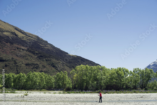 Excursionista de rojo frente a un bosque y montañas en Nueva Zelanda