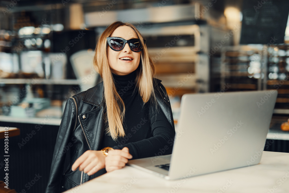 Young girl sit in coffee place in front of the window, wear glasses, look at her laptop and drink tea from red cup Young girl sit in coffee place in front of the window, wear glasses, look at her laptop and drink tea from red cup