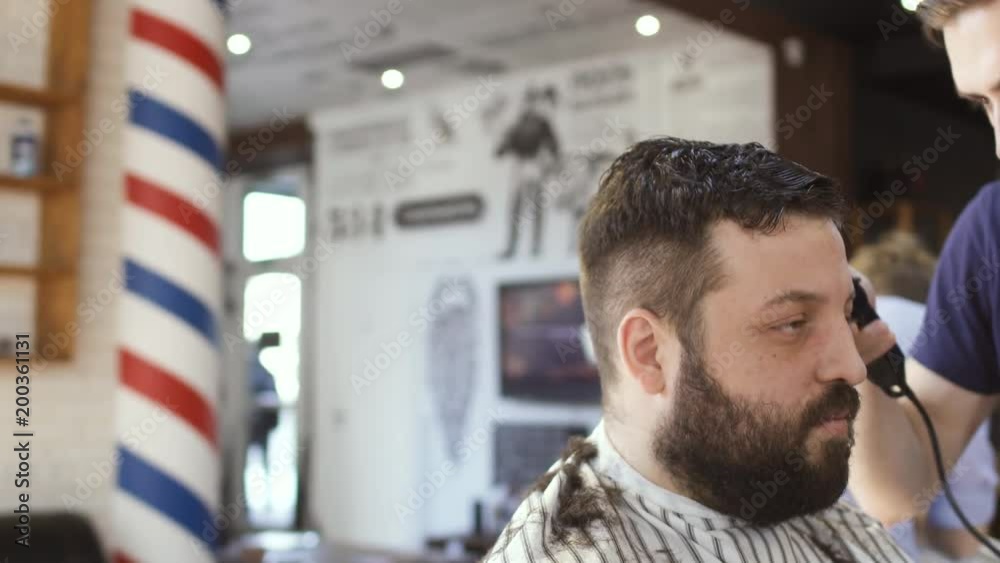 Hairdresser makes hairstyle to a young bearded man Hairdresser makes hairstyle to a young bearded man