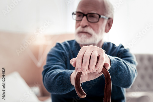 Senior age. Selective focus of elderly mans hands being put on the walking stick while holing it