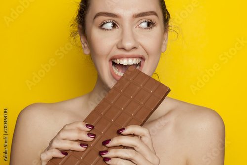 young happy woman enjoying eating chocolate on a yellow background