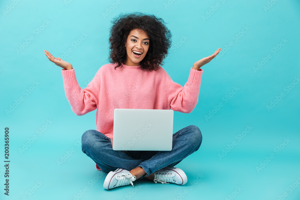 Optimistic woman with beautiful smile using silver notebook, while sitting in lotus pose on the floor and throwing hands aside, isolated over blue background Optimistic woman with beautiful smile using silver notebook, while sitting in lotus pose on the floor and throwing hands aside, isolated over blue background