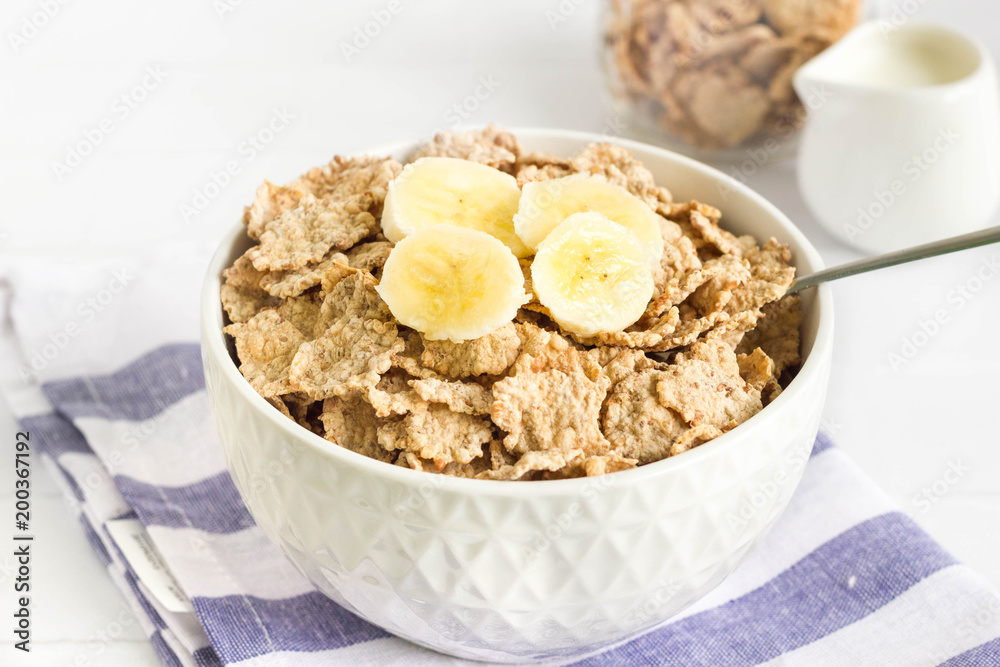 Whole wheat cornflakes with banana slices in white bowl Whole wheat cornflakes with banana slices in white bowl