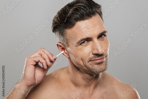 Handsome mature man holding cotton bud take care of his ears cleaning it.