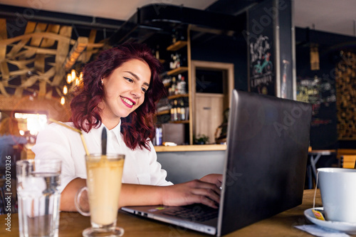Portrait of happy young pretty woman with a laptop at cafe.Woman sitting in coffee shop with a laptop.