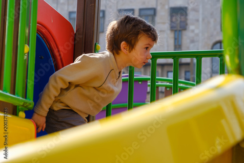 Cute caucasian child boy having fun to play slider in the playground