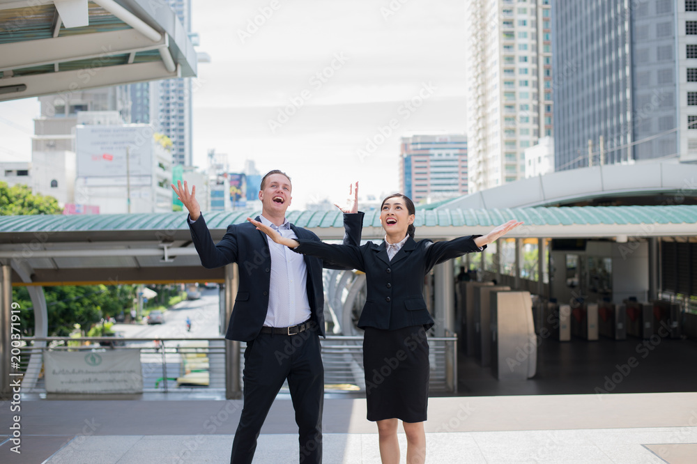 Asian businessman and businesswoman stand and raising up two hands to cheerful and celebrated for successful in career and mission. concept of winner and competition. Asian businessman and businesswoman stand and raising up two hands to cheerful and celebrated for successful in career and mission. concept of winner and competition.
