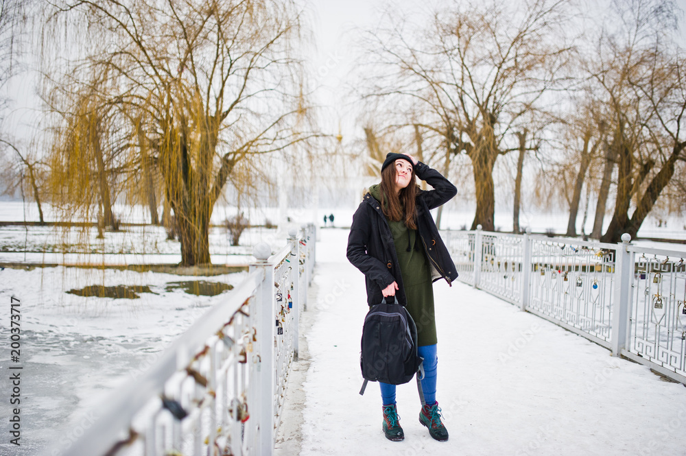 Young girl wear on long green sweatshirt, jeans and black headwear with backpack in winter day.