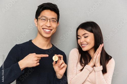 Cheerful young asian loving couple holding bitcoin.