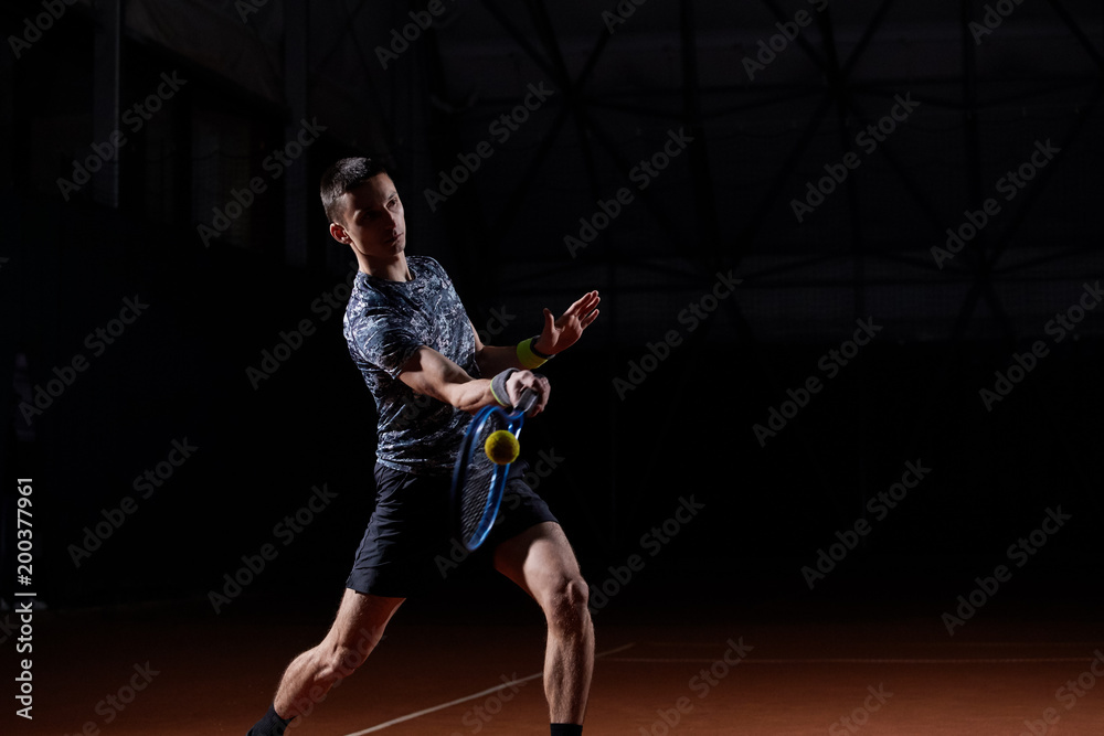young professional tennis player with a blue racket hitting a forehand, black background young professional tennis player with a blue racket hitting a forehand, black background