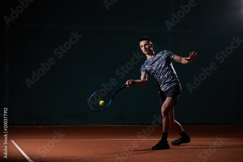 young professional tennis player with a blue racket hitting a forehand, black background © Mircea.Netea