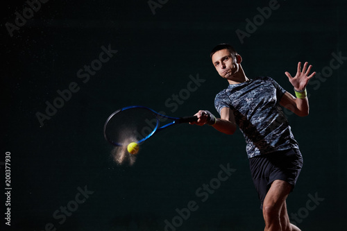young professional tennis player with a blue racket hitting a forehand, black background, wet ball creating a splash © Mircea.Netea