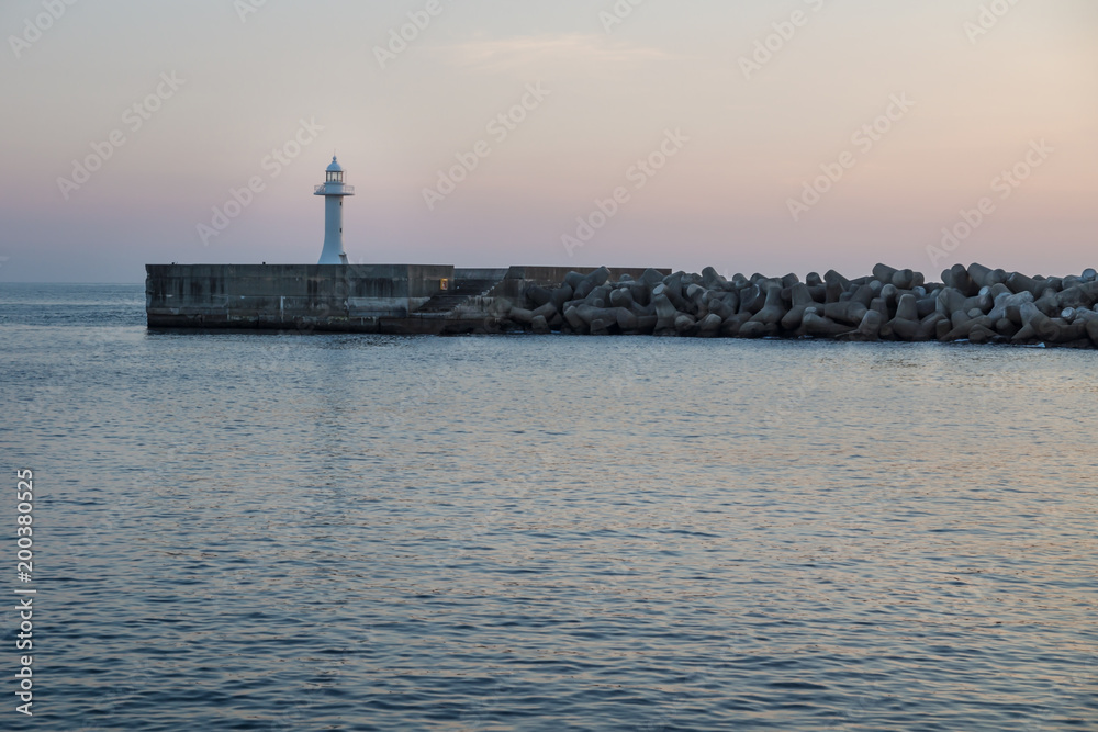 Seawall with wavebreakers with white lighthouse during dawn in Seogwipo, Jeju Island, South Korea