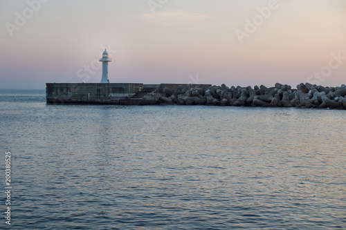 Seawall with wavebreakers with white lighthouse during dawn in Seogwipo, Jeju Island, South Korea