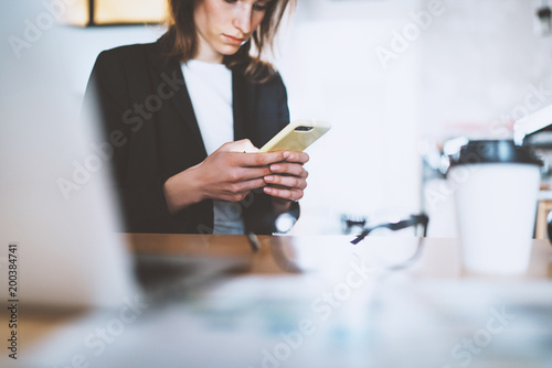 Attractive young businesswoman typing text message on smartphone while working at office.Blurred background.