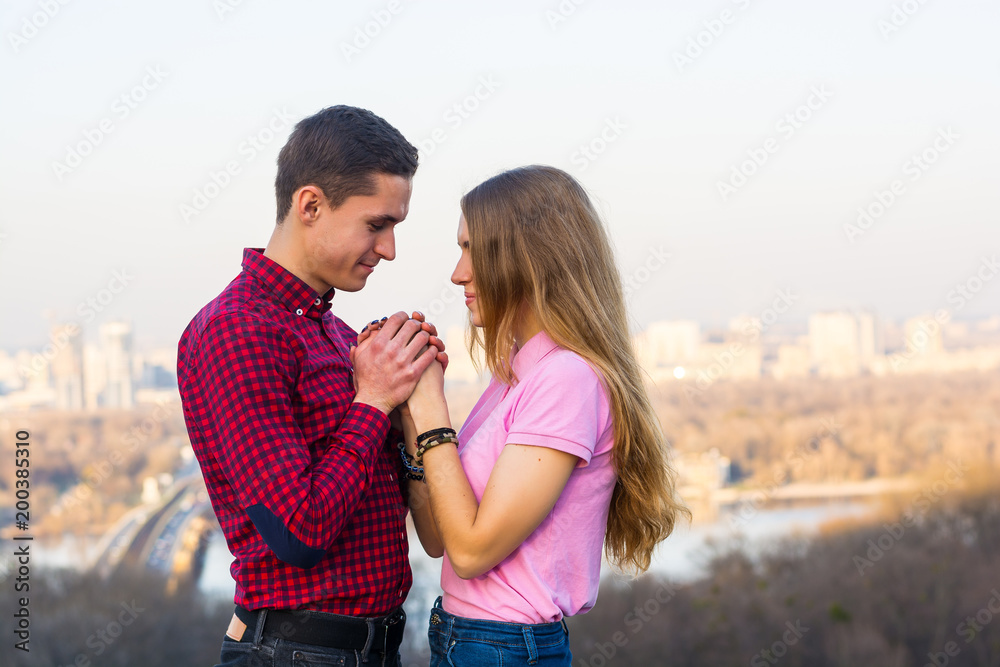 Fototapeta premium The guy holds the girl's hands in his against the backdrop of the cityscape