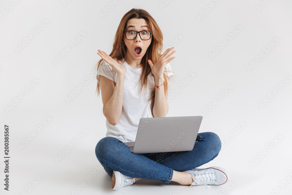Naklejka premium Shocked woman in t-shirt and eyeglasses sitting on the floor