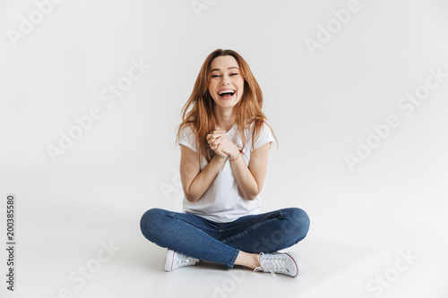 Pleased woman in t-shirt sitting on floor with arms together