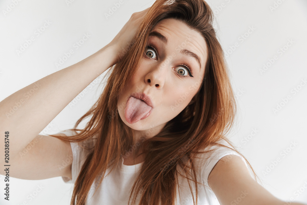Funny woman in casual clothes making selfie while showing tongue Funny woman in casual clothes making selfie while showing tongue