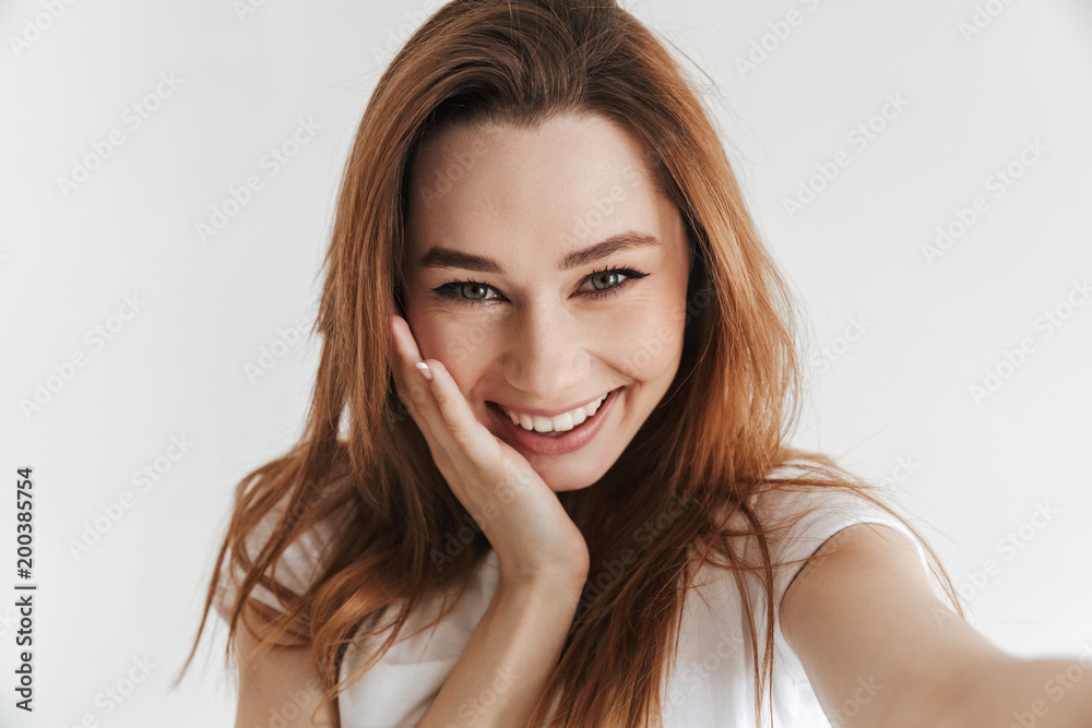 Pleased woman in casual clothes making selfie while holding cheek Pleased woman in casual clothes making selfie while holding cheek