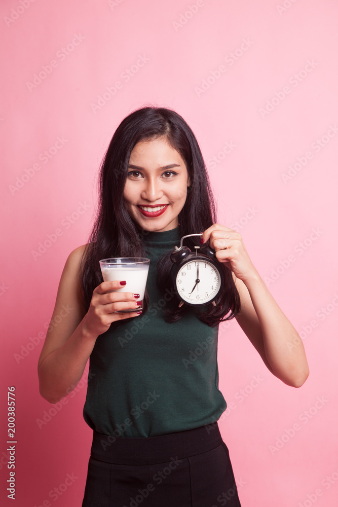 Fototapeta premium Healthy Asian woman drinking glass of milk hold clock.