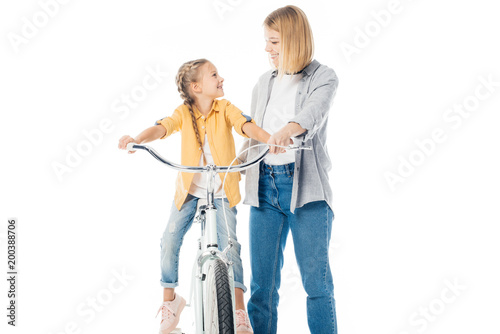 smiling mother and cute daughter on bicycle looking at each other isolated on white