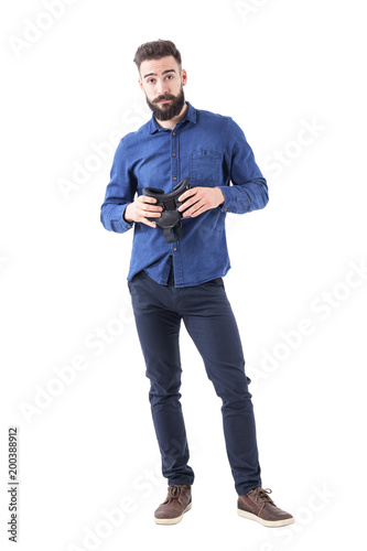 Confused skeptical indifferent business man holding virtual reality headset looking at camera. Full body isolated on white background. 