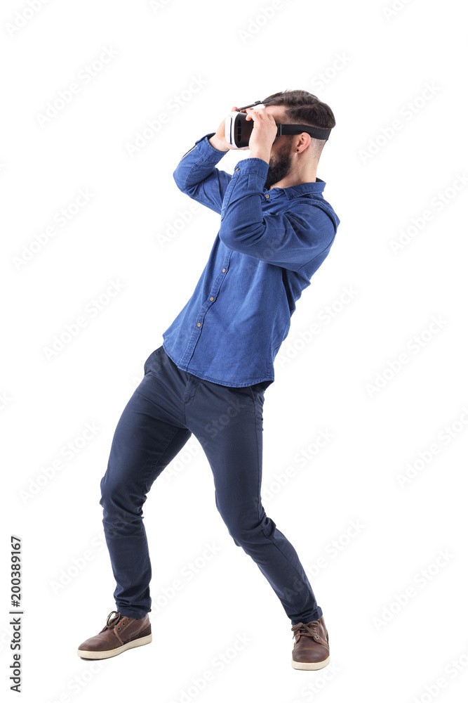 Side view of bending young man having virtual reality goggles experience. Full body isolated on white studio background. Side view of bending young man having virtual reality goggles experience. Full body isolated on white studio background.