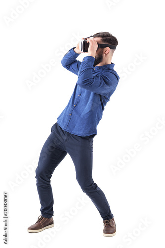 Side view of bending young man having virtual reality goggles experience. Full body isolated on white studio background. 