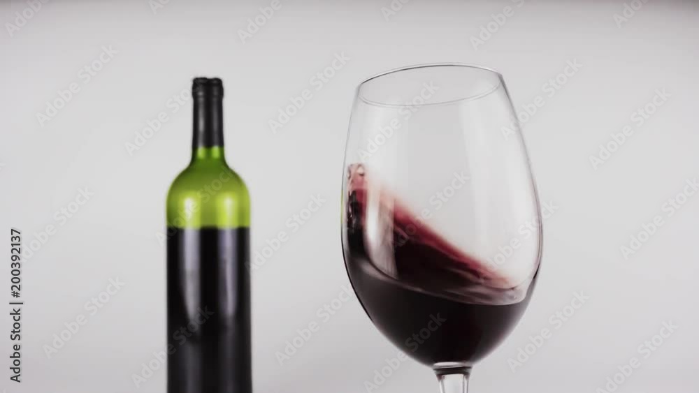 A glass of red wine in a hand on a white background. In the background is a bottle of wine. 4k A glass of red wine in a hand on a white background. In the background is a bottle of wine. 4k