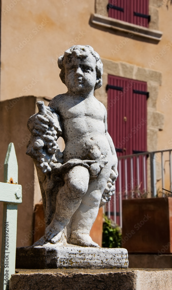 Statue of Bacchus (Dionysus) with grapes in his hands against rough stone wall. Garden sculpture. (Provence, France)