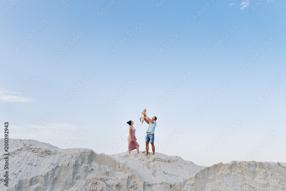 Happy family together, parents with their little baby boy on sand. Father raising baby up in the air
