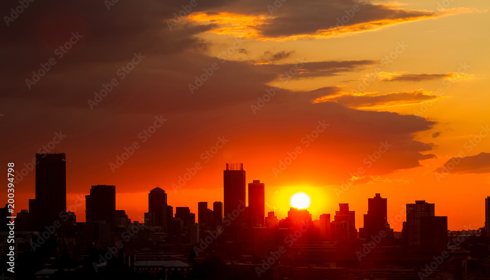 Dramatic cloudy sky at sunset in urban area. Silhouette buildings and lens flare from the sun