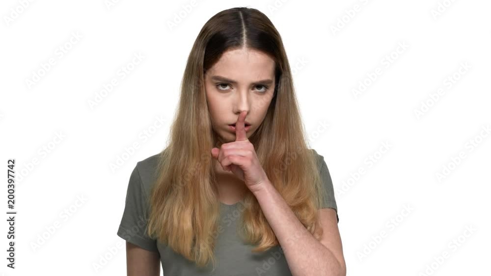 Portrait of severe brunette woman with dyed hair holding index finger on lips and asking to keep quiet, isolated over white background. Concept of emotions