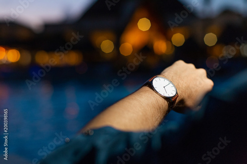 A man at a fancy resort checks his watch at nighttime and thinks about the end of his vacation
