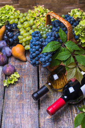 Red wine in a bottle and white wine bottle, cork, bottle screw and a set of products - cheese, grapes, nuts, pears, plums, flowers, figs, white bread, baguette on a wooden board, background