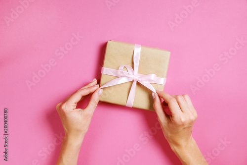Young woman holding bunch of presents wrapped in hand made blank craft paper gift wrap, satin bow. Female hands, simple giftbox, wrapping, giftwrap, silk ribbon. Pink background, close up, copy space. © Evrymmnt