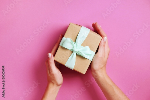Young woman holding bunch of presents wrapped in hand made blank craft paper gift wrap, satin bow. Female hands, simple giftbox, wrapping, giftwrap, silk ribbon. Pink background, close up, copy space.