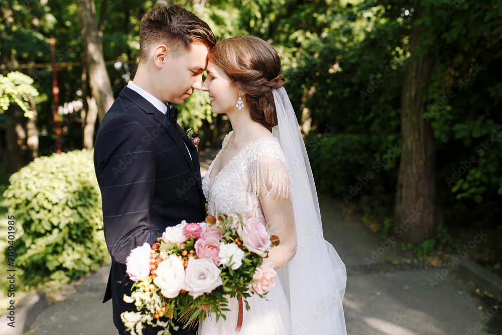 Happy Couple of Bride and groom in a park kissing. Happy newlyweds at wedding in nature green forest are kissing photo portrait.Wedding Happy Couple of Bride and groom in a park kissing. Happy newlyweds at wedding in nature green forest are kissing photo portrait.Wedding