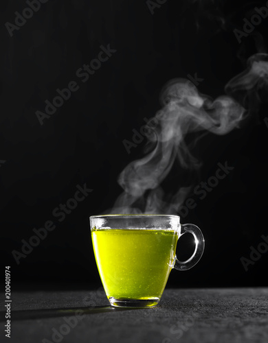 Freshly brewed green tea in a transparent glass Cup,escaping steam,darker background.