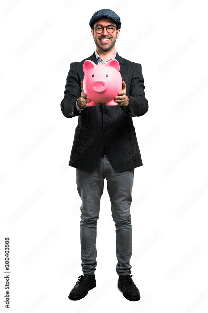 Handsome modern man with beret and glasses holding a piggybank Handsome modern man with beret and glasses holding a piggybank