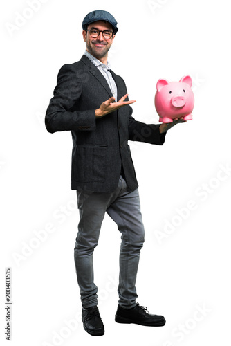 Handsome modern man with beret and glasses holding a piggybank