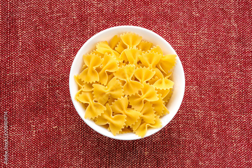 farfalle macaroni pasta in a white cup on a red brown rustic texture background, in the center close-up from the top.