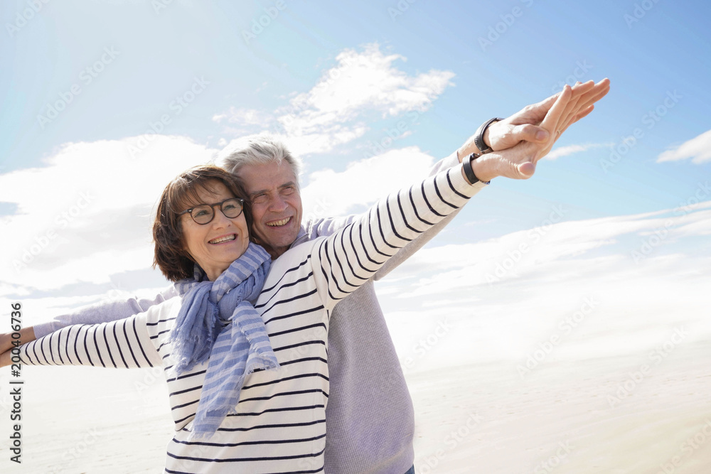 Portrait of senior couple at the beach stretching arms out Portrait of senior couple at the beach stretching arms out