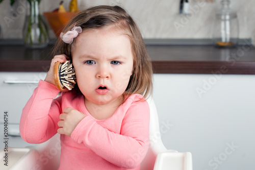 Schilderij op canvas girl 2 years old playing with a comb at home - portraying an emotional conversat