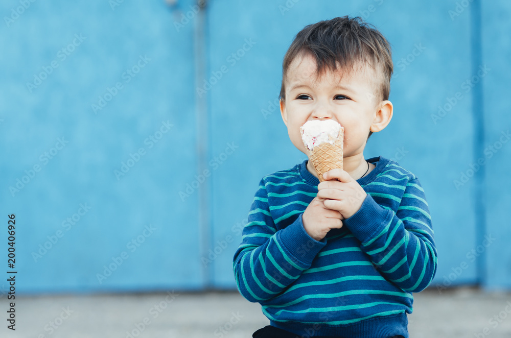 Fototapeta premium baby outdoor on blue wall background eating ice cream