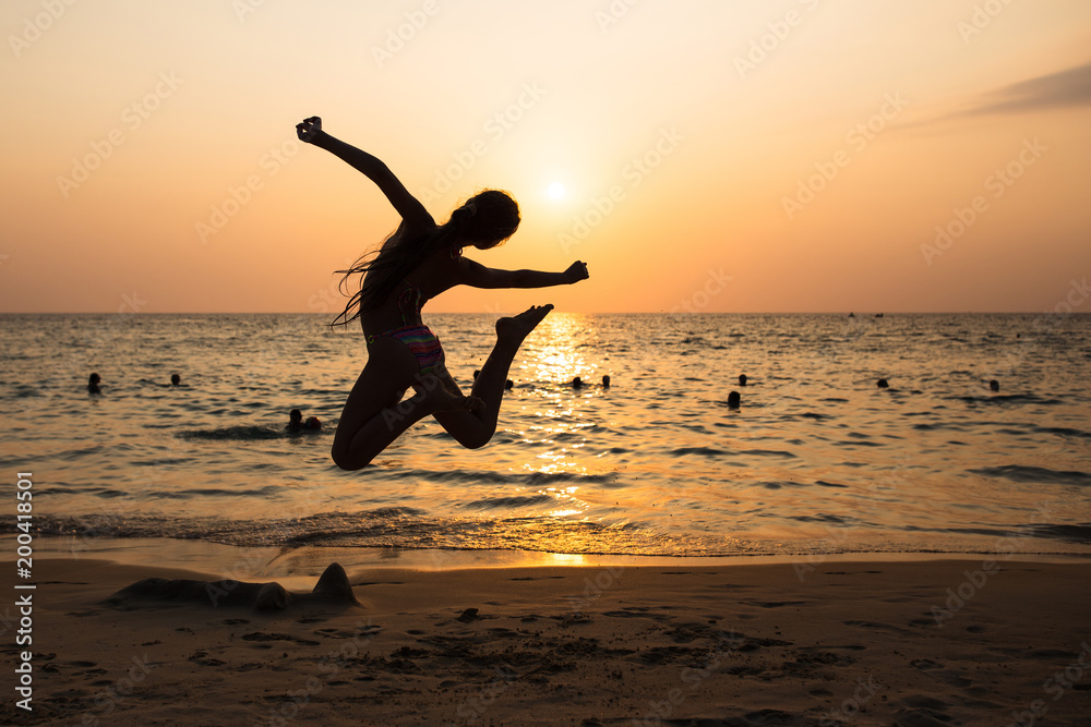 Woman jumping and having fun at the beach against the sunset