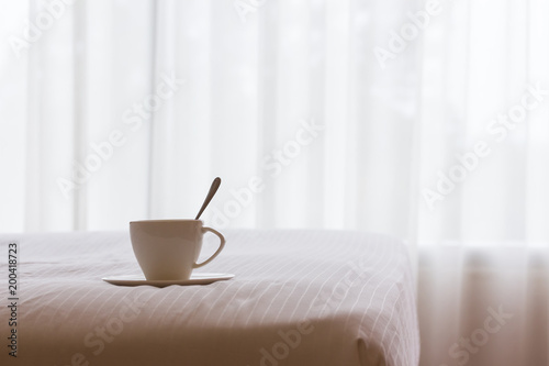 White coffee cup on the bed in the morning.