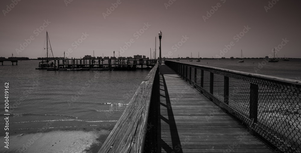 Wooden pier at Gulfport, Florida with sailboats in the bay, monochrome