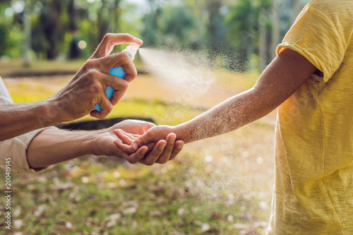 dad and son use mosquito spray.Spraying insect repellent on skin outdoor photo